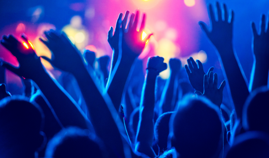 A group of people with raised hands at a concert. They are bathed in a blue light.
