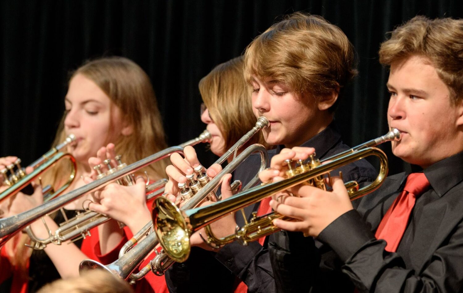 A group of children play trumpets at a concert. Two are boys and two are girls.