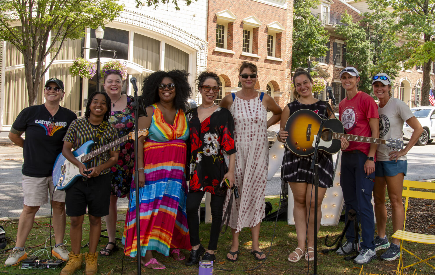 A diverse group of women, some holding instruments, pose for a photo outdoors in front of a building.